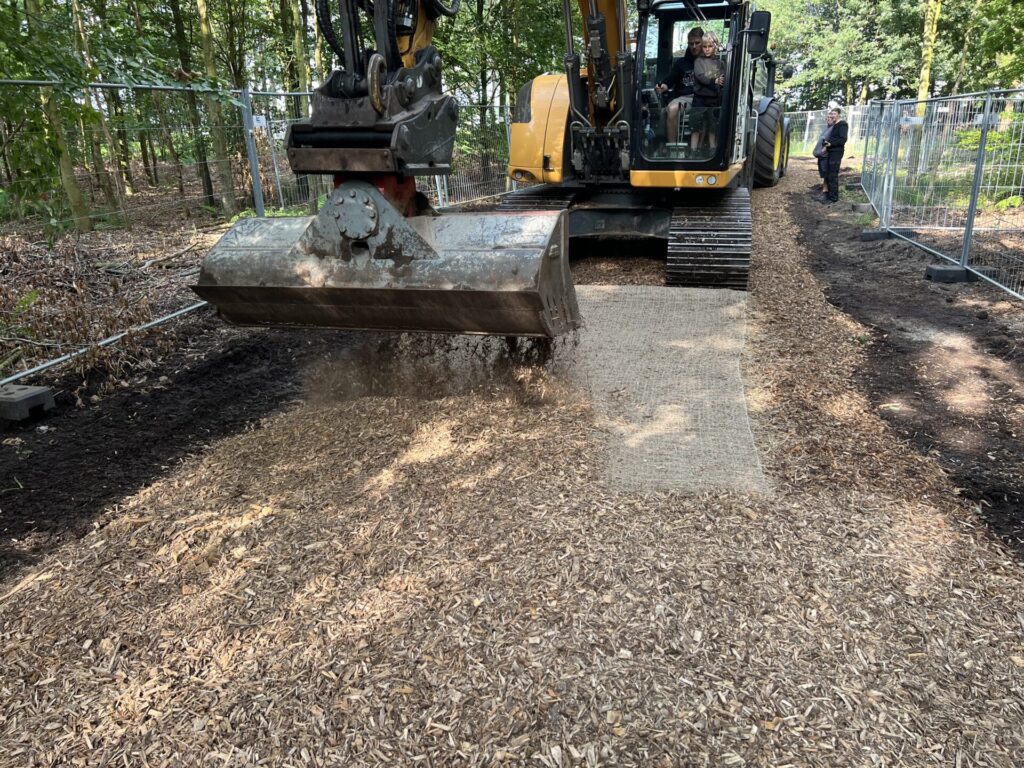 Bagger verteilt Holzschnitze auf der Bodenschutzmatte