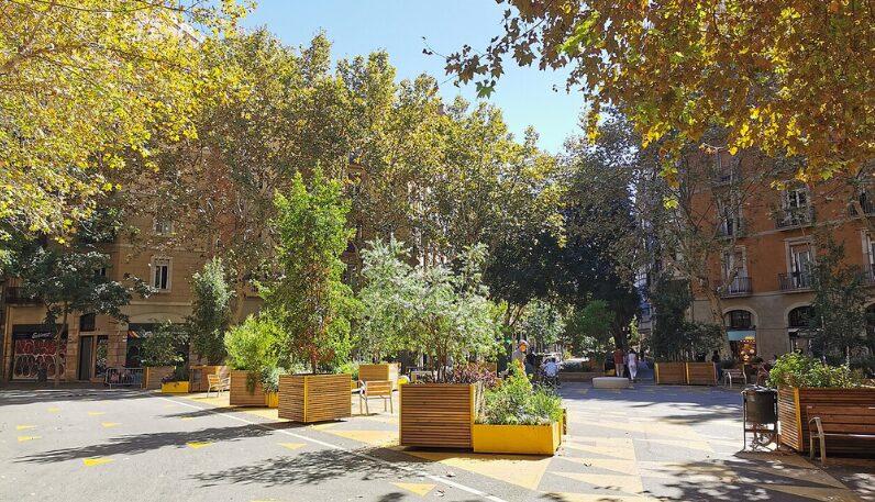 Barcelona: Auf einer Straße mit dreieckigen Markierungen stehen Hochbeete und Bäume.