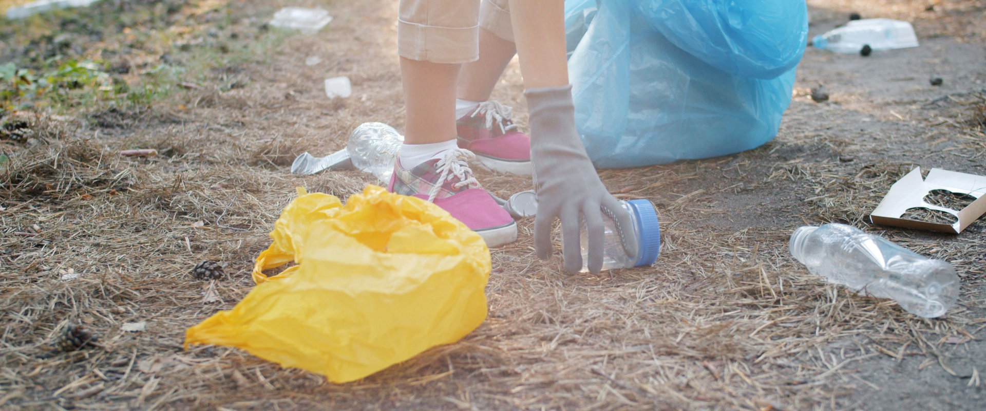 Müll auf sandigem Boden. Eine Hand hebt einen Plastikbecher auf.