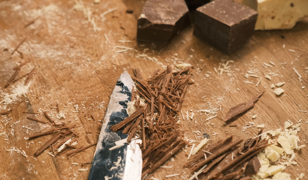 Schokolade klein geschnitten auf einem Brettchen mit Messer.